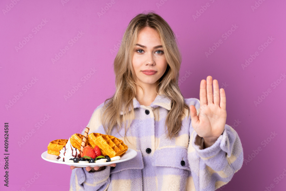 Teenager Russian girl holding waffles isolated on purple background making stop gesture Teenager Russian girl holding waffles isolated on purple background making stop gesture