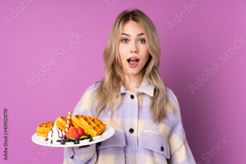 Teenager Russian girl holding waffles isolated on purple background with surprise facial expression