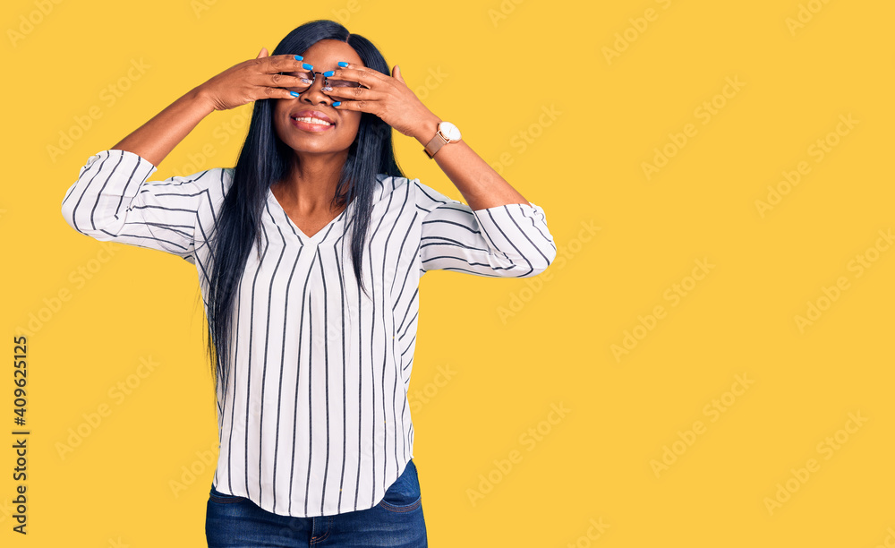 Naklejka premium Young african american woman wearing casual clothes and glasses covering eyes with hands smiling cheerful and funny. blind concept.