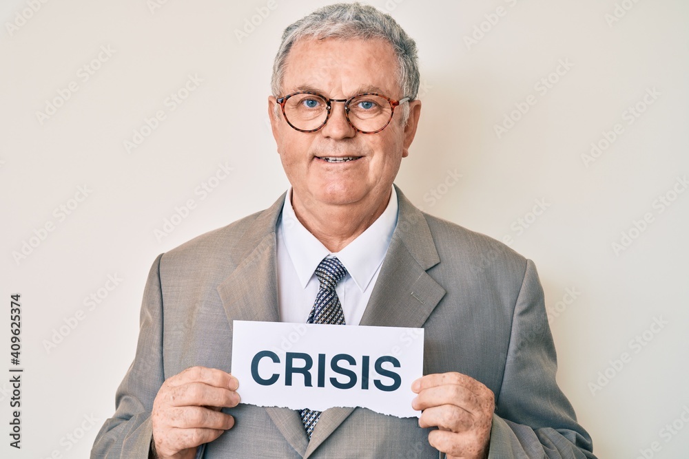 Senior grey-haired man wearing business suit holding crisis paper smiling with a happy and cool smile on face. showing teeth. Senior grey-haired man wearing business suit holding crisis paper smiling with a happy and cool smile on face. showing teeth.