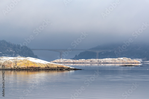 Snow covered island in sunlight with nice reflection in the water on Swedish west coast with no buildings or people. Bridge from town Stenungsund to island Tjörn in background photo