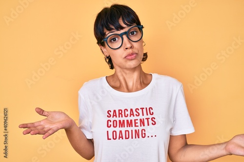 Beautiful brunettte woman wearing sarcastic comments loading t-shirt clueless and confused expression with arms and hands raised. doubt concept. photo