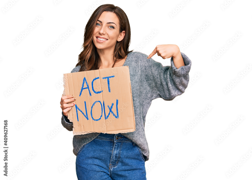Young brunette woman holding act now banner pointing finger to one self smiling happy and proud Young brunette woman holding act now banner pointing finger to one self smiling happy and proud