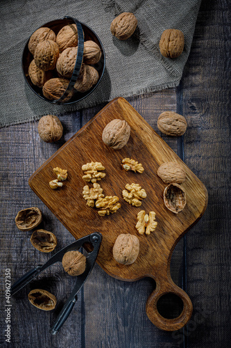 Whole and cracked walnuts, nutcracker on wooden board and background