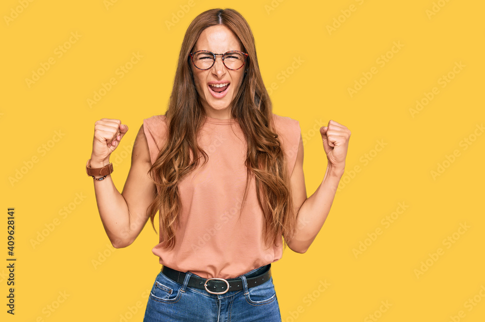 Young hispanic woman wearing casual clothes and glasses angry and mad raising fists frustrated and furious while shouting with anger. rage and aggressive concept. Young hispanic woman wearing casual clothes and glasses angry and mad raising fists frustrated and furious while shouting with anger. rage and aggressive concept.