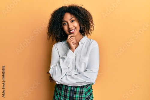 Beautiful african american woman with afro hair wearing scholar skirt looking confident at the camera with smile with crossed arms and hand raised on chin. thinking positive. © Krakenimages.com