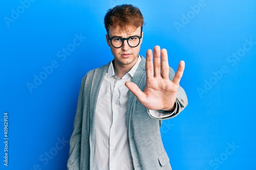 Young caucasian man wearing elegant clothes and glasses doing stop sing with palm of the hand. warning expression with negative and serious gesture on the face.