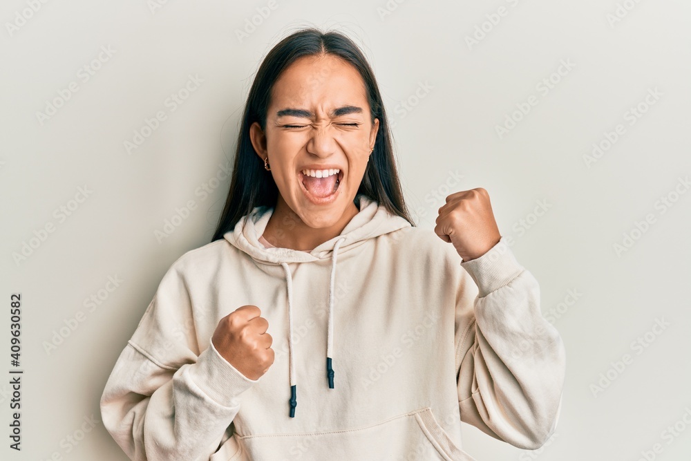 Young asian woman wearing casual sweatshirt celebrating surprised and amazed for success with arms raised and eyes closed Young asian woman wearing casual sweatshirt celebrating surprised and amazed for success with arms raised and eyes closed