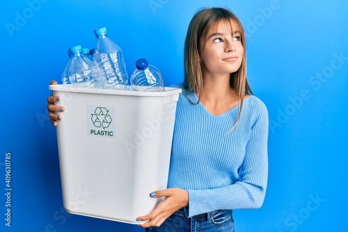 Teenager caucasian girl holding recycling bag with plastic bottles smiling looking to the side and staring away thinking.