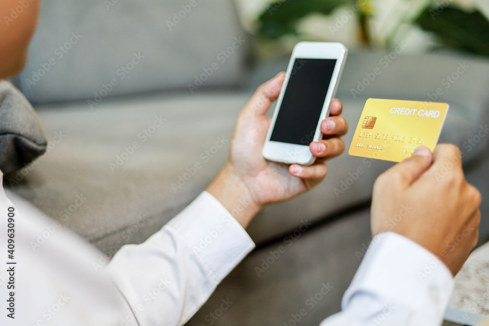 Man holding a moblie phone and a gold credit card, he is filling out credit card information on his phone to work, pay bills online, online shopping ideas.