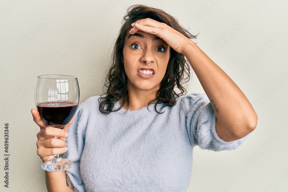 Young hispanic woman drinking a glass of red wine stressed and frustrated with hand on head, surprised and angry face Young hispanic woman drinking a glass of red wine stressed and frustrated with hand on head, surprised and angry face