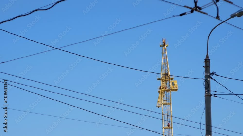 Urban view of lamp posts and electric wires against the sky of a construction crane during the construction of a multi-storey sky building. Urban view of lamp posts and electric wires against the sky of a construction crane during the construction of a multi-storey sky building.
