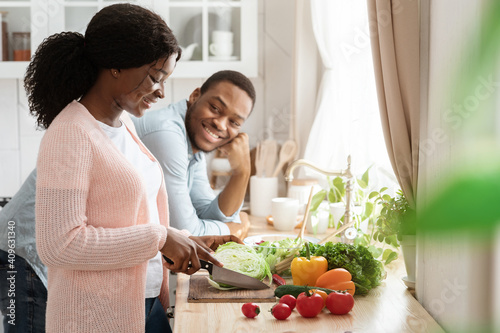 Smiling black couple cooking in kitchen together, preparing healthy vegetable meal