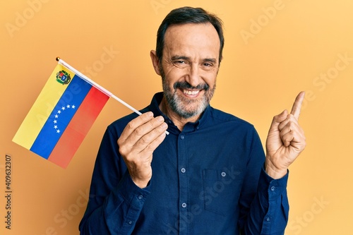 Middle age hispanic man holding venezuelan flag smiling happy pointing with hand and finger to the side