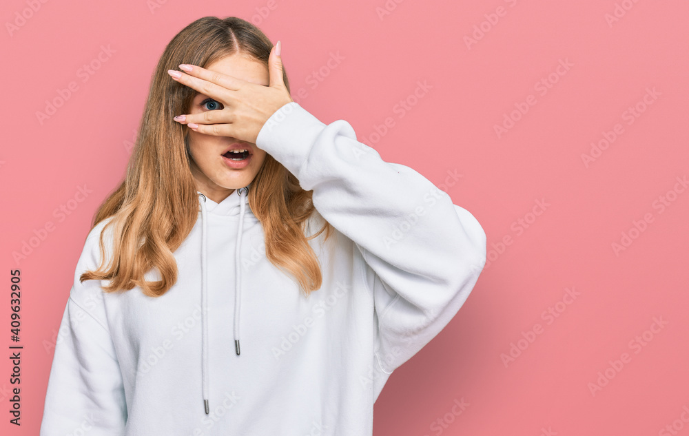 Beautiful young caucasian girl wearing casual sweatshirt peeking in shock covering face and eyes with hand, looking through fingers with embarrassed expression. Beautiful young caucasian girl wearing casual sweatshirt peeking in shock covering face and eyes with hand, looking through fingers with embarrassed expression.