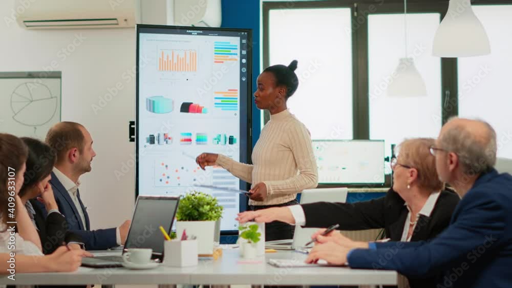 African american coach giving corporate presentation for businesspeople in office, businesswoman explaning business plan on digital board, speaking to clients at meeting working in boardroom.