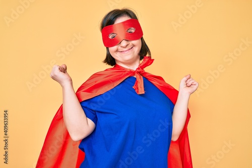 Brunette woman with down syndrome wearing super hero costume very happy and excited doing winner gesture with arms raised, smiling and screaming for success. celebration concept.