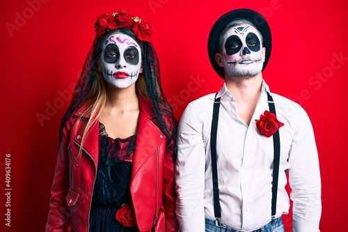 Couple wearing day of the dead costume over red relaxed with serious expression on face. simple and natural looking at the camera.