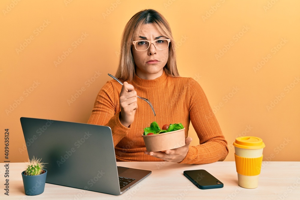 Young caucasian woman working at the office eating healthy salad skeptic and nervous, frowning upset because of problem. negative person. Young caucasian woman working at the office eating healthy salad skeptic and nervous, frowning upset because of problem. negative person.