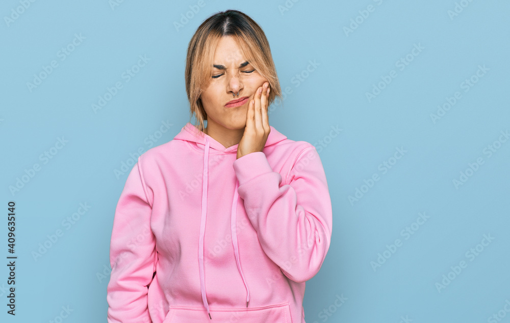 Young caucasian woman wearing casual sweatshirt touching mouth with hand with painful expression because of toothache or dental illness on teeth. dentist Young caucasian woman wearing casual sweatshirt touching mouth with hand with painful expression because of toothache or dental illness on teeth. dentist