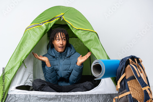 Young african american man inside a camping green tent holding copyspace with two hands