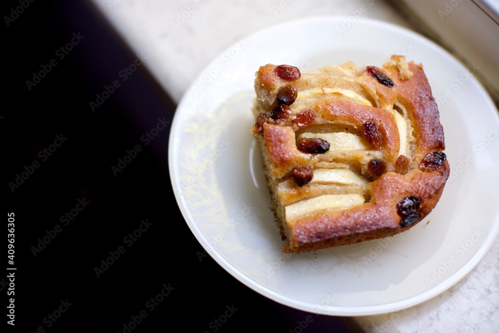 piece of cake with raisins and apples with natural light near the window. blurry view