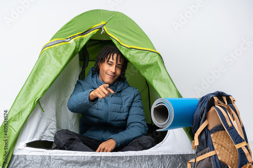 Young african american man inside a camping green tent points finger at you with a confident expression