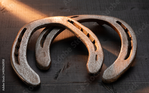 Old worn and rusty two horseshoes on a black wooden background in the evening sun
