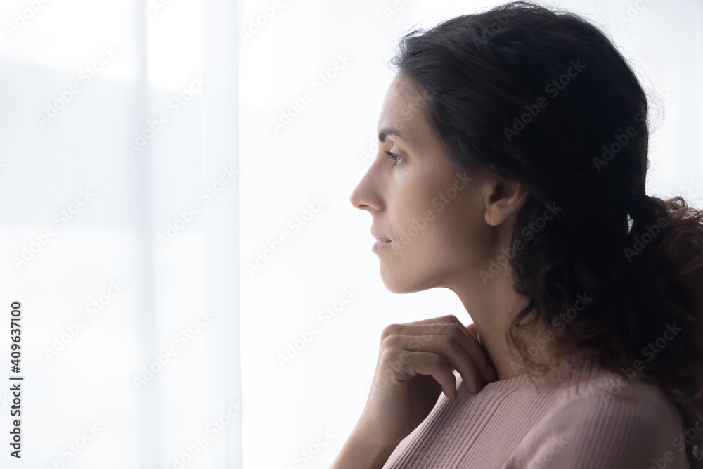 Head shot side view thoughtful young caucasian woman standing near window, looking in distance, thinking of difficult personal problems solutions, felling melancholic alone indoors, copy space.