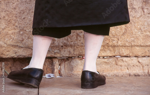 Western Wall, Jerusalem: close-up on the legs of Hasidic Jewish man in traditional dress of white socks and black leather shoes under long silk suit photo