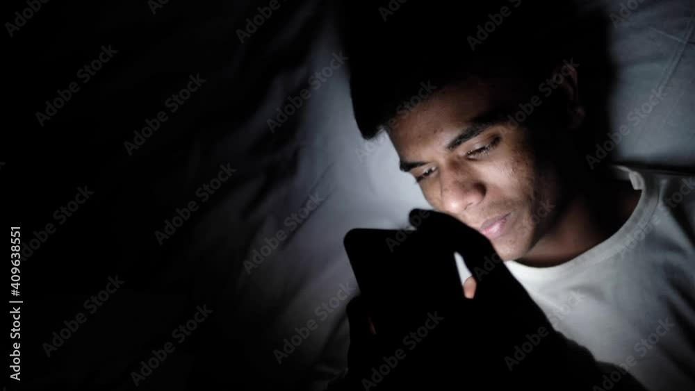 young man sitting on bed using smart phone at night young man sitting on bed using smart phone at night