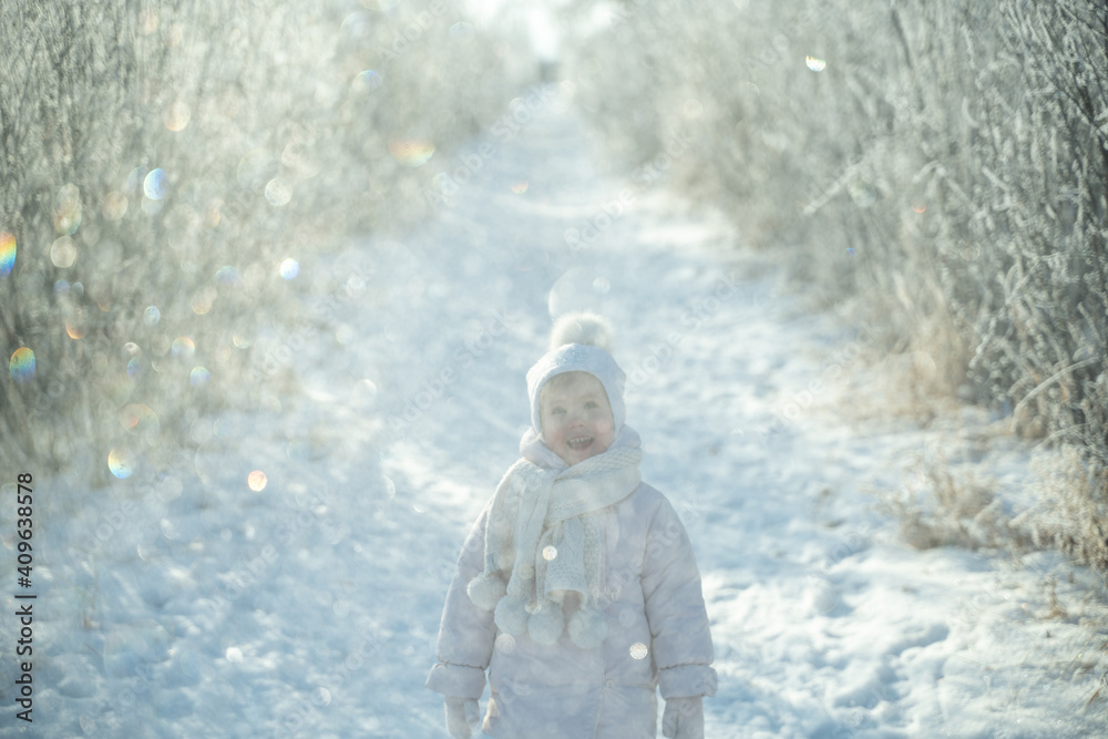 A child in a warm white hat and scarf plays with snow while walking in the winter forest, snowfall, winter magic, bright emotion, protecting the skin from frost A child in a warm white hat and scarf plays with snow while walking in the winter forest, snowfall, winter magic, bright emotion, protecting the skin from frost