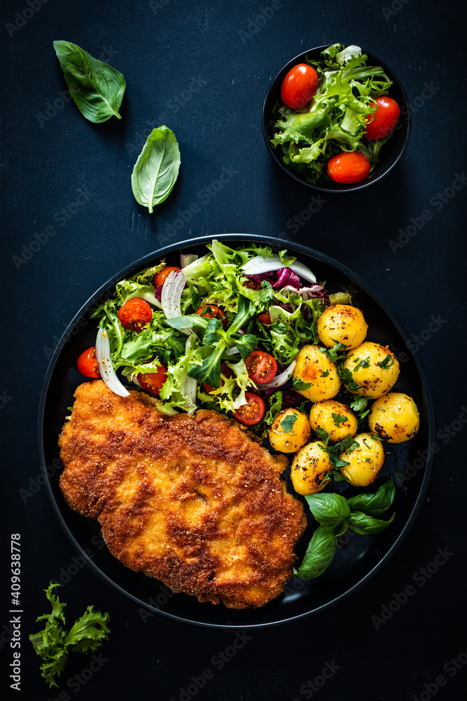 Breaded fried pork chop, French fries and vegetables on white background

