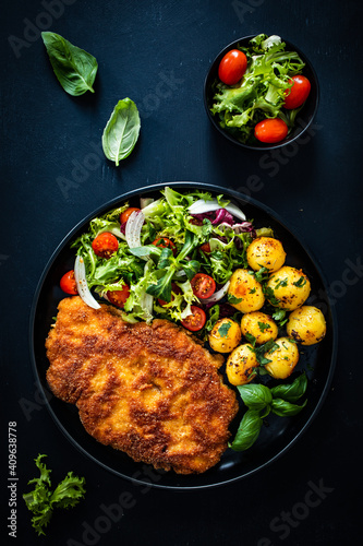 Breaded fried pork chop, French fries and vegetables on white background 
