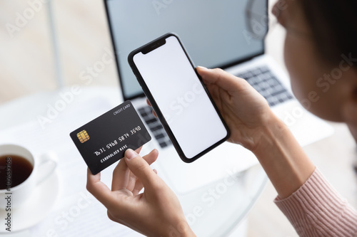 Close up young woman holding bank credit card and modern tech device with mock up white screen in hands, enjoying purchasing goods in internet store using mobile phone application, online shopping. photo