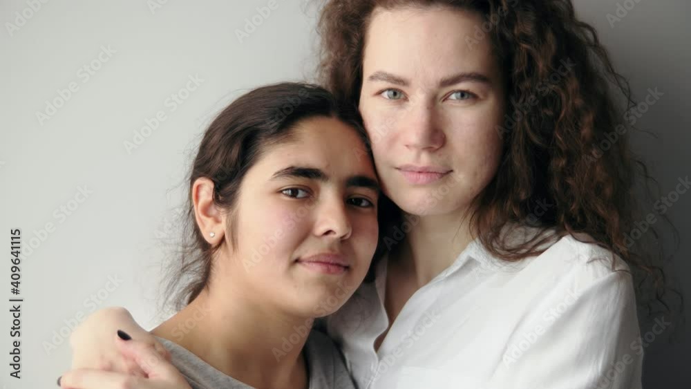 Curly haired european woman hugs middle eastern race child girl. Two girls of different races are looking at the camera embracing Curly haired european woman hugs middle eastern race child girl. Two girls of different races are looking at the camera embracing