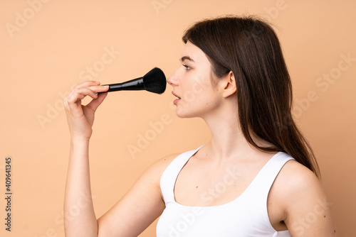 Young Ukrainian teenager girl over isolated background holding makeup brush