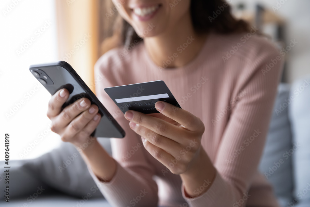 Close up smiling millennial woman holding smartphone and banking credit card, involved in online mobile shopping at home, happy female shopper purchasing goods or services in internet store. Close up smiling millennial woman holding smartphone and banking credit card, involved in online mobile shopping at home, happy female shopper purchasing goods or services in internet store.