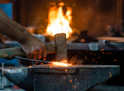 Fotografie, Obraz Close up blacksmith working metal with hammer on the anvil in the forge