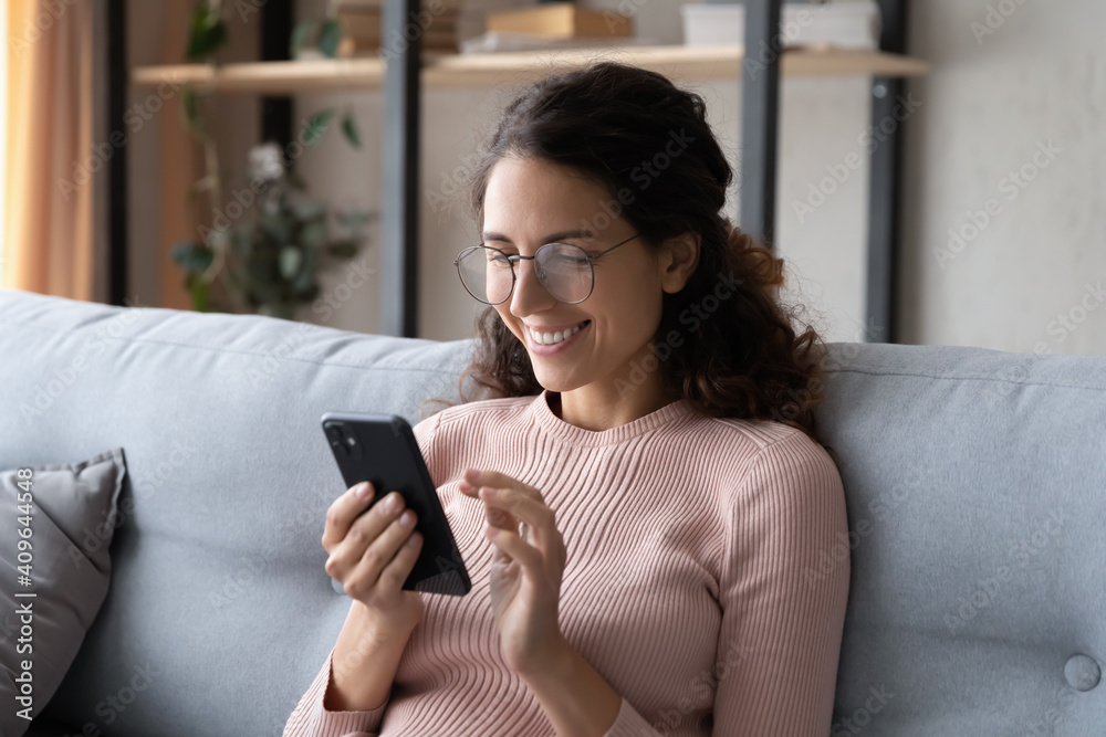 Happy millennial woman relaxing on comfortable sofa, enjoying web surfing information in internet or using mobile software application, communicating distantly with friends in social networks at home. Happy millennial woman relaxing on comfortable sofa, enjoying web surfing information in internet or using mobile software application, communicating distantly with friends in social networks at home.