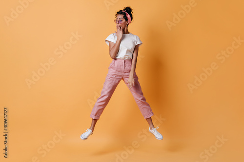 Shocked woman in pink pants jumping and looking away. Full length view of amazed mixed race girl.