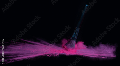 Pink makeup powder brush fall on shiny black surface in a dust cloud