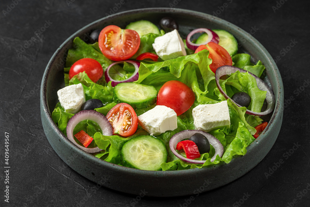 Greek salad with fresh vegetables, feta cheese and olives in a plate on black background. Vegetarian healthy food