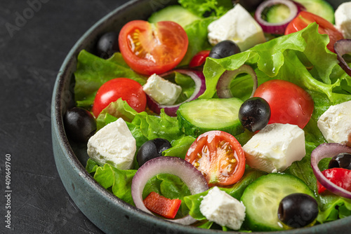 Close up of Greek salad with fresh vegetables, feta cheese and olives in a plate on black background. Vegetarian food