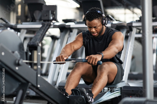 Motivated black sportsman having workout on rowing machine