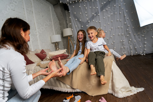 Mom in the bedroom on the bed fun tickles the legs of children, boys and girls. photo