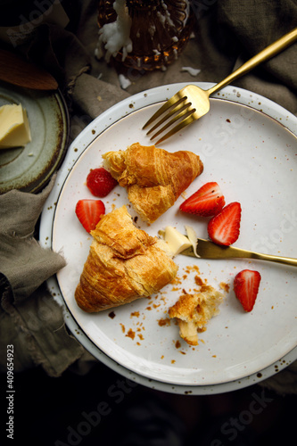 pieces of croissant on a white plate with strawberries and golden cutlery