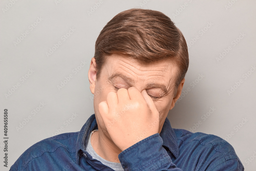 Portrait of unhappy tired man touching bridge of nose, squinting eyes Portrait of unhappy tired man touching bridge of nose, squinting eyes