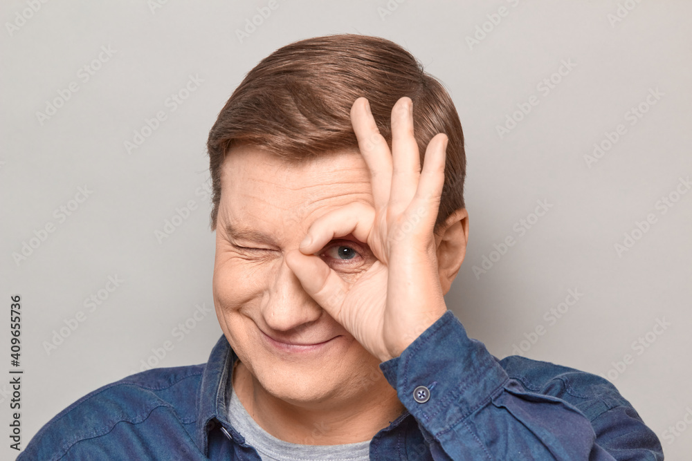 Portrait of happy mature man showing okay gesture near eye Portrait of happy mature man showing okay gesture near eye