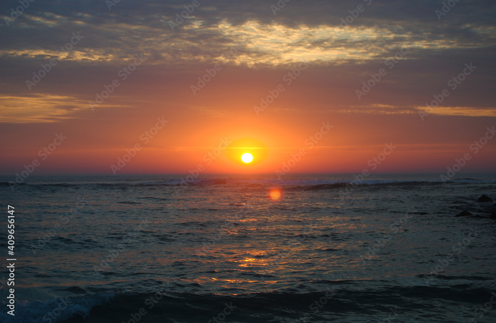 Por-do-sol na praia com nuvens no céu em várias cores alaranjadas e tons de branco